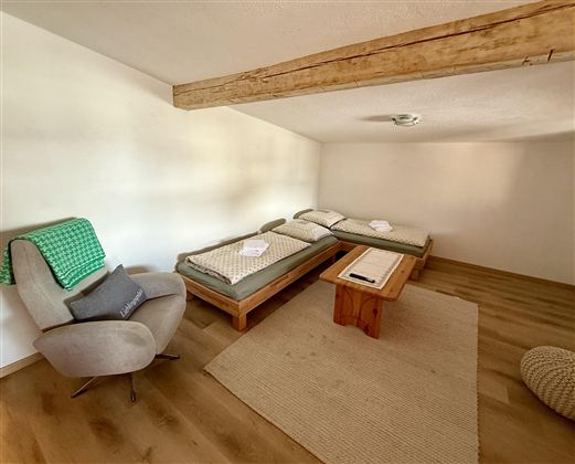 Ein ruhiger Raum mit zwei Betten und einem Holz-Geschirr. Eine gemütliche Sitzecke und ein Teppich runden das dezente Ambiente ab.