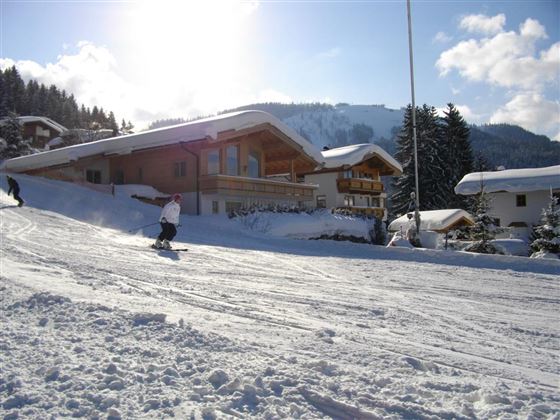Eine verschneite Landschaft mit Skifahrern und chalets. Der Himmel ist blau und die Sonne scheint.