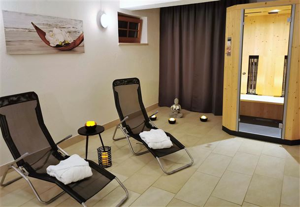 Ein entspannender Wellnessbereich mit zwei Liegen und sanfter Beleuchtung. Im Hintergrund ist eine Sauna zu sehen, die zur Ruhe und Erholung einlädt.