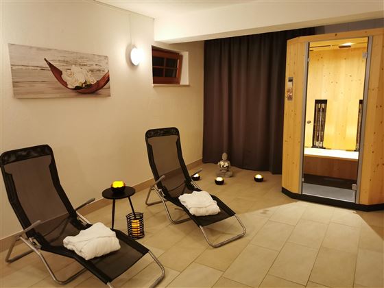 Ein entspannender Wellnessbereich mit zwei Liegen und einer Sauna. Sanfte Beleuchtung und dekorative Elemente schaffen eine ruhige Atmosphäre.