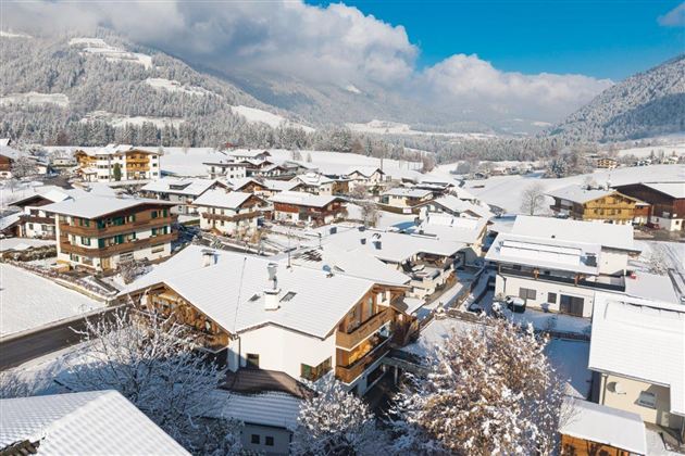 Ein malerisches winterliches Dorf mit schneebedeckten Häusern. Die umliegenden Berge und der klare Himmel verleihen der Szene eine friedliche Atmosphäre.