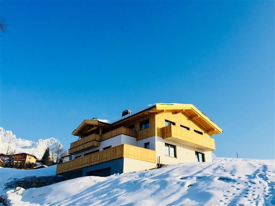 Ein modernes Haus mit einem gelben Holzverkleidung in einer verschneiten Landschaft. Der klare blaue Himmel bildet einen schönen Hintergrund.