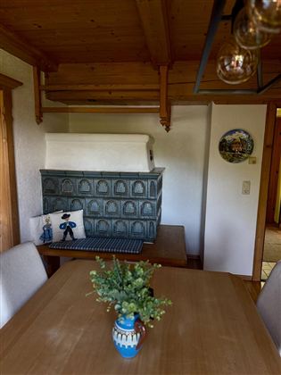 A cozy room with a wood stove and a dining table. On the table, there is a vase with flowers, and small decorative figures are visible.