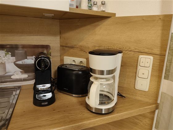 Een moderne keukenoek met een koffiemachine, een broodrooster en een espressomachine. Het meubilair is van licht hout en creëert een uitnodigende sfeer.