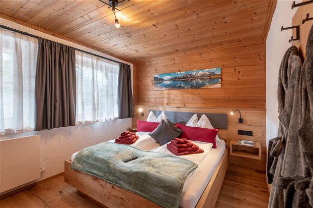 Ein gemütliches Schlafzimmer mit einem großen Bett und Holzwänden. Weiche Decken und Kissen in warmen Farben schaffen eine einladende Atmosphäre.