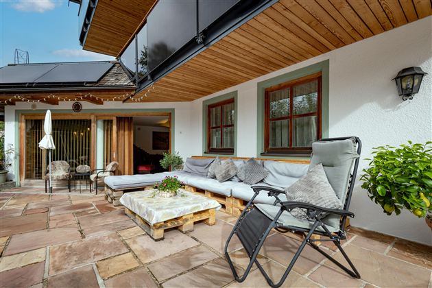 Eine gemütliche Terrasse mit Sitzgelegenheiten und einem modernen Holzüberstand. Die Umgebung ist hell und einladend, ideal zum Entspannen.