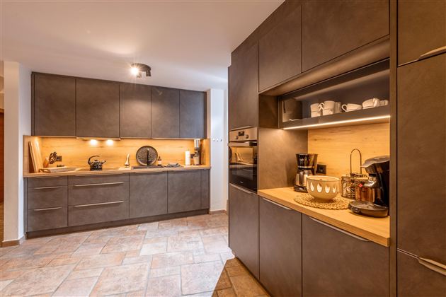 Eine moderne Küche mit dunklen Schränken und einer hellen Holzoberfläche. Die Beleuchtung sorgt für eine gemütliche Atmosphäre.