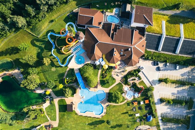 A large complex with several swimming pools and slides surrounded by green meadows. The building has an attractive architecture and invites relaxation.