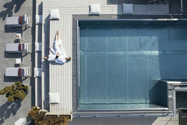 Een modern zwembad met ligstoelen op een terras. Een persoon ontspant zich in een badjas naast het water.