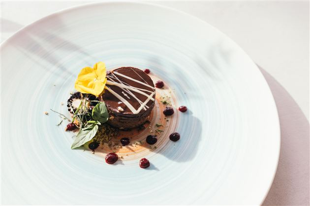 Een kunstzinnig gepresenteerd dessert op een blauwe schaal. De chocoladetaart is versierd met een bloemetje en bessen.