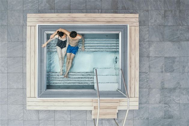 Een stel zit ontspannen in een moderne jacuzzi. Het gebied is helder en uitnodigend ingericht, omgeven door grijze tegels.