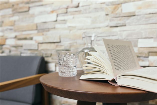 Een Open boek ligt op een ronde houten tafel. Naast het boek staan een glas water en een kan, voor een mooie stenen muur.