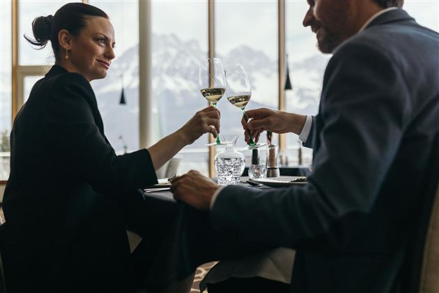 Een paar proost in een elegant restaurant met champagneglazen. Op de achtergrond zijn besneeuwde bergen te zien.