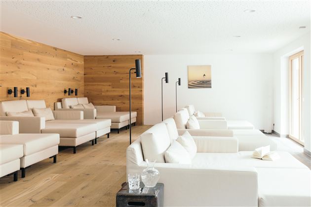 Een stijlvolle ontspanningsruimte met comfortabele, lichte ligstoelen en een bijpassende houten afwerking. Grote ramen zorgen voor veel daglicht en een rustige sfeer.