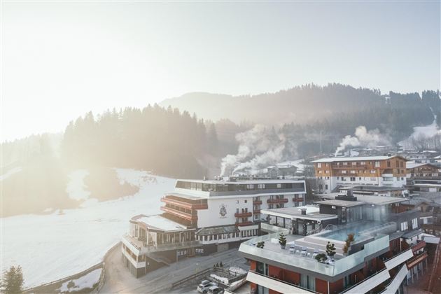Een besneeuwd berglandschap met moderne chalets en rokende schoorstenen. De heldere lucht en de glooiende heuvels creëren een rustige en uitnodigende sfeer.