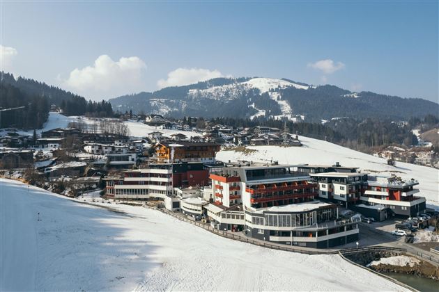 Een pittoresk berglandschap met besneeuwde heuvels. Op de voorgrond zijn moderne gebouwen te zien dicht bij een skipiste.