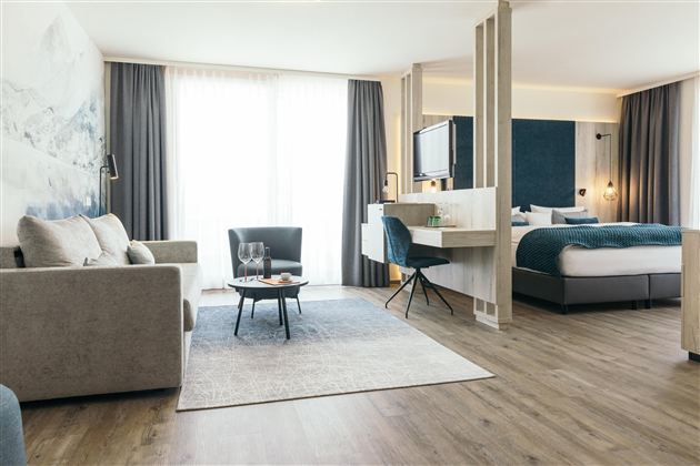 Een moderne hotelkamer met een comfortabele bank en een groot raam dat veel licht laat binnenkomen. De elegante inrichting en de rustige kleuren creëren een uitnodigende sfeer.