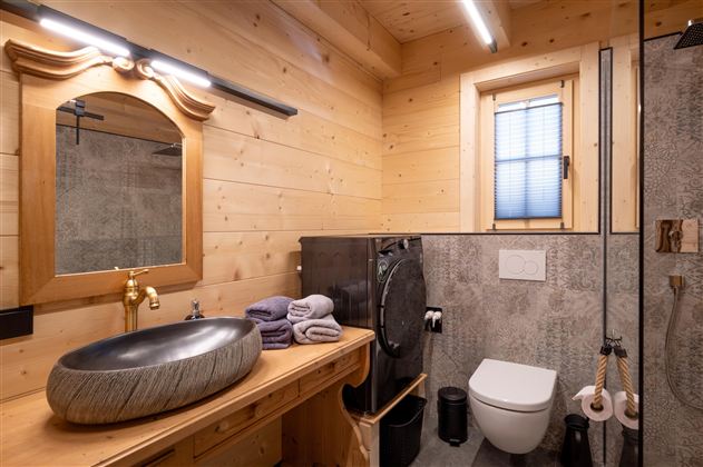Een moderne badkamer met houten wanden en elegante fittingen. Het bevat een wastafel, toiletten en een douche.