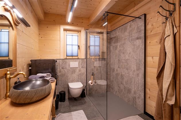 Een moderne badkamer met houten panelen en een grote glazen douche. De wastafel is stijlvol en rond, en er zijn ramen die voor natuurlijk licht zorgen.