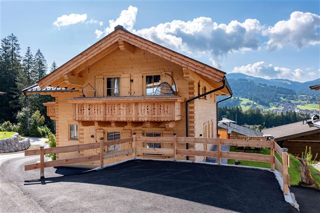 Een traditioneel chalet van hout in een schilderachtige berglandschap. De omgeving is groen met mooie bergen op de achtergrond.