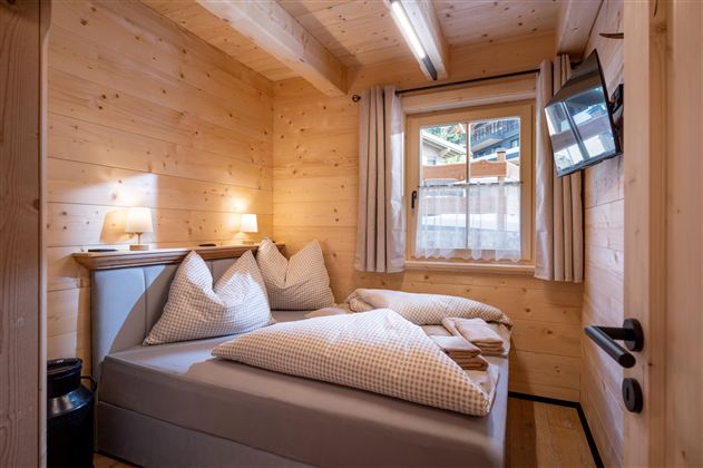 Een gezellige slaapkamer met houten wandpanelen, een tweepersoonsbed en grote kussens. De kamer heeft een raam met uitzicht naar buiten en een televisie aan de muur.