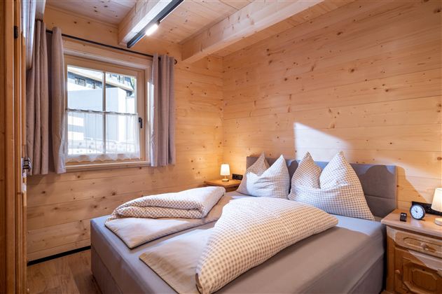 Een gezellig slaapkamer met houten wandpanelen en een groot bed. Er zijn kussens en een kleine nachttafel lamp naast het bed.