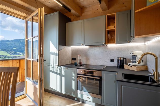 Een moderne keuken met lichte kasten en een balkonuitzicht op de bergen. De ruimte is goed verlicht en biedt een gezellige sfeer.