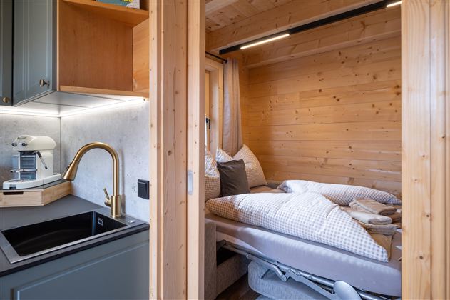 Een gezellige houten kamer met een bed en een moderne keukenhoek. Het licht is warm en creëert een uitnodigende sfeer.