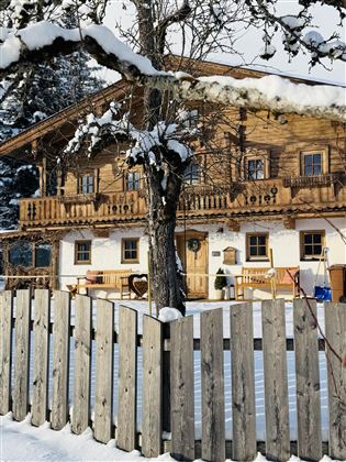 A cozy wooden house in the snow, surrounded by a wooden picket fence. The scene conveys a calm winter atmosphere.