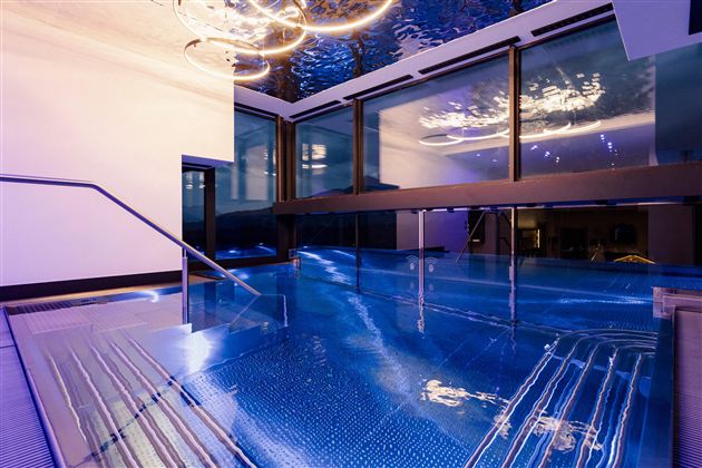 Een elegante binnenzwembad met een blauwe, reflecterende wateroppervlak. Grote ramen en stijlvolle verlichting creëren een ontspannende sfeer.