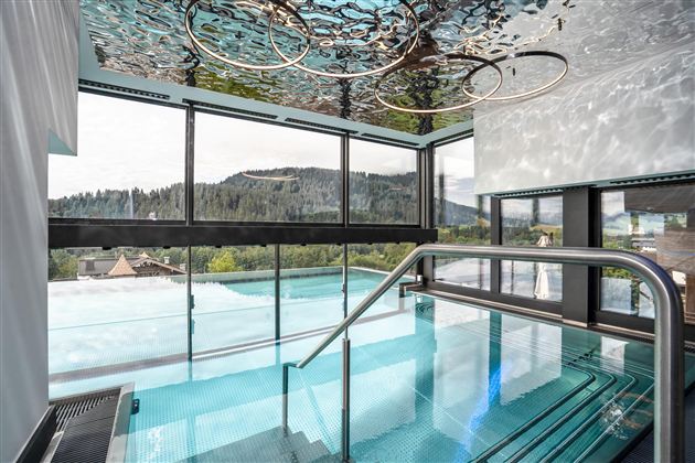 Een modern zwembad met glazen front en uitzicht op groene heuvels. Het water weerkaatst de omgeving en creëert een ontspannende sfeer.