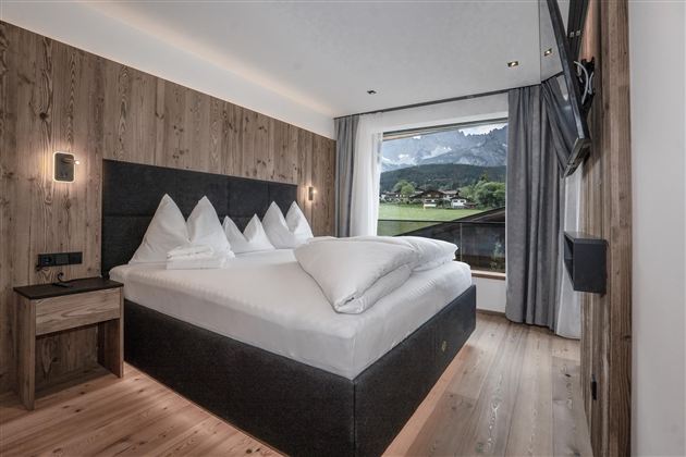 Een moderne hotelkamer met een groot tweepersoonsbed en uitzicht op het bos. De muren zijn van hout, en de kamer is licht en uitnodigend.