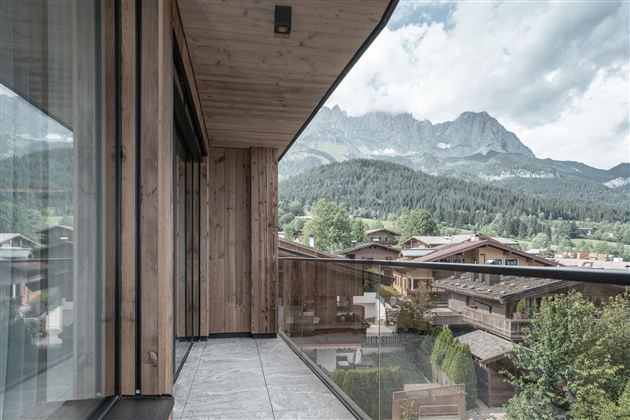 Een modern balkon met houten bekleding en uitzicht op groene bergen. Het landschap wordt gekenmerkt door een rustige en natuurlijke sfeer.