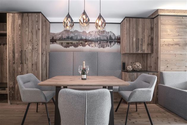 Een moderne eetkamer met een houten tafel en comfortabele stoelen. De muren zijn in warme houttinten gehouden, en boven de tafel hangen stijlvolle lampen.