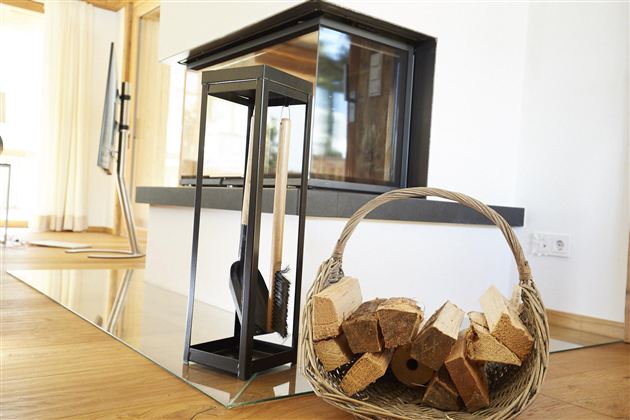 Ein moderner Kamin mit klaren Linien steht in einem hellen Raum. Neben dem Kamin befindet sich ein Korb mit Holzscheiten.