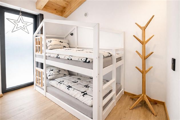 Ein modernes Kinderzimmer mit einem Etagenbett und weißen Bettwäsche, die mit Pandas bedruckt ist. An der Wand steht ein Holzkleiderständer und es gibt ein Fenster mit einem dekorativen Stern.