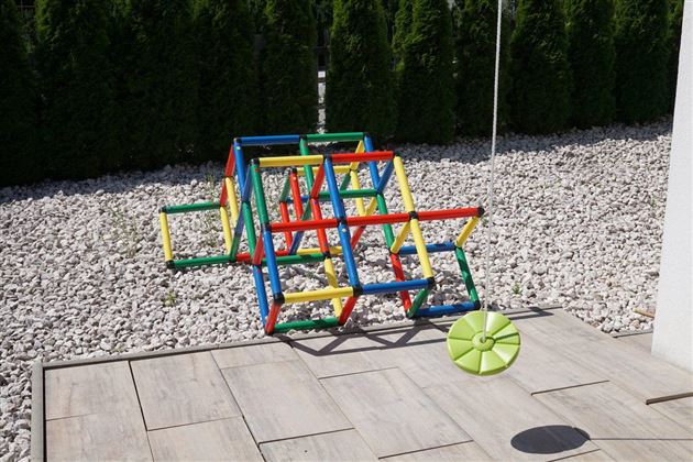 Een kleurrijk klimrek van kunststof staat in de tuin op een grindbed. Naast het klimrek ligt een groene bal.