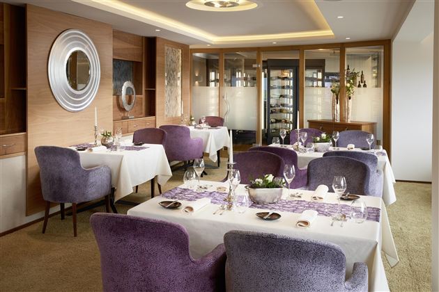 An elegant restaurant with modern furniture and set tables. The walls are designed with warm wood tones and stylish accents.