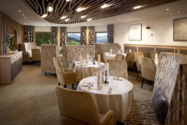An elegant restaurant with cozy tables and chairs. Large windows offer a view of the green landscape.