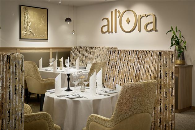 An elegant restaurant with modern dining areas and stylish furniture. The tables are elegantly decorated and there are plants to enhance the ambiance.