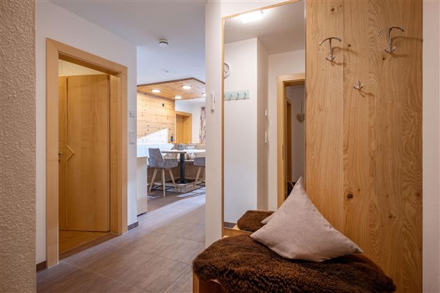 Een moderne gang met houten meubels en een gezellige zithoek. Op de achtergrond zijn een eetgedeelte en een goed verlichte ruimte zichtbaar.