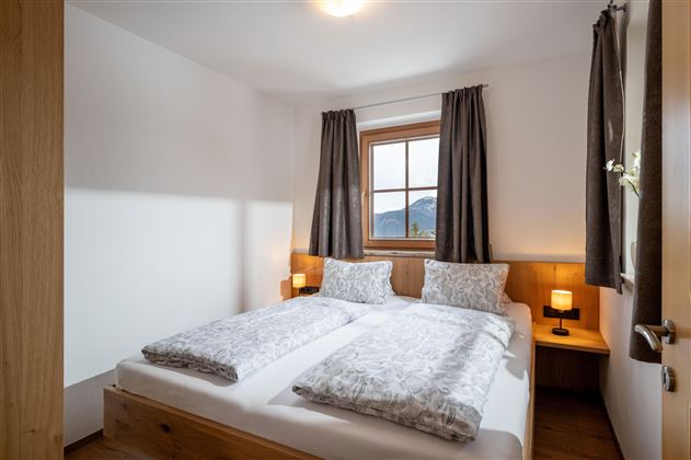 Een gezellige slaapkamer met twee bedden en een grote glazen wand. De inrichting is modern en licht, met houten details en zachte kleuren.