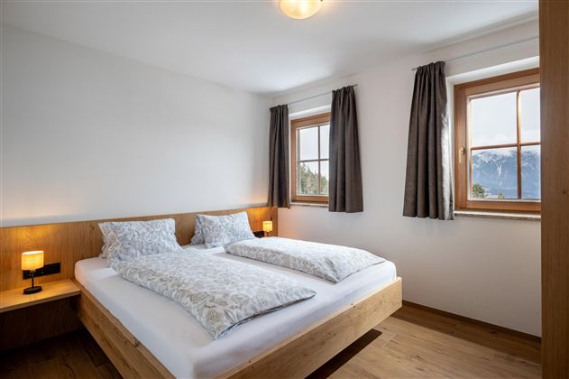 Een lichte slaapkamer met twee bedden en grote ramen. Houten details en gordijnen zorgen voor een gezellige sfeer.