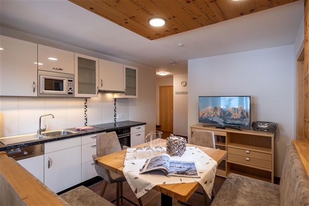 Een moderne woning met een open keuken en eetgedeelte. De ruimte is licht en uitnodigend, met een televisie en gezellige meubels.