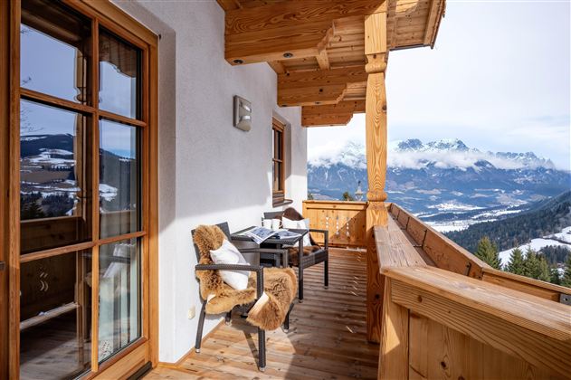 Een mooie balkon met houten bekleding en twee gezellige stoelen. Op de achtergrond zijn besneeuwde bergen en een heldere lucht te zien.