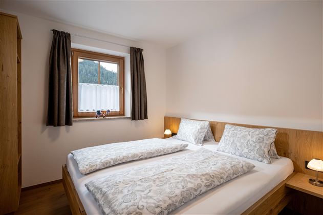 Een gezellig slaapkamer met een tweepersoonsbed en twee nachtkastjes. Grote ramen met gordijnen zorgen voor natuurlijk licht.