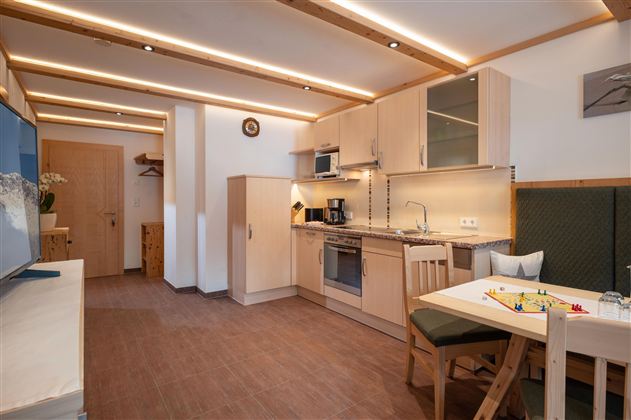 Een moderne keuken met lichte kasten en een eethoek. De ruimte is goed verlicht en vriendelijk ingericht.