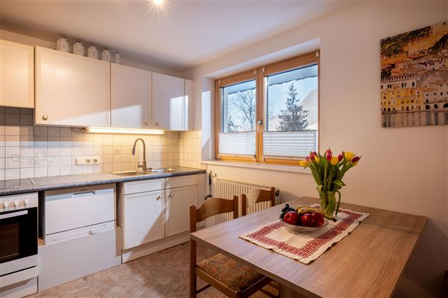 Ein einfacher Essbereich mit einem Holz Tisch und einer Eckbank. Auf dem Tisch liegt eine graue Sitzauflage, und an der Wand hängt ein Bild.