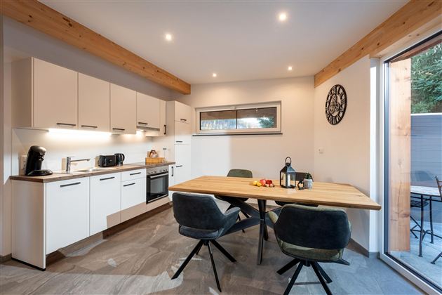 Eine moderne Küche mit einem großen Tisch und stilvollen Stühlen. Das Licht betont die hellen Wände und die Holzdetails.