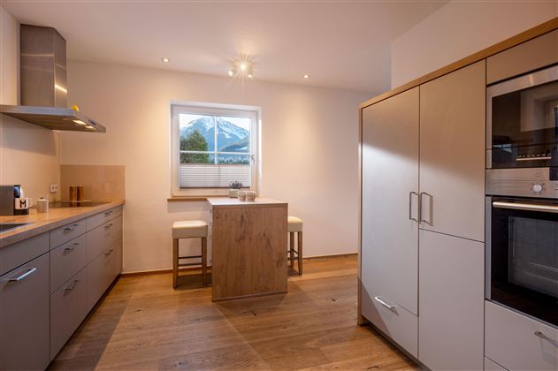 Eine moderne Küche mit hellen Schränken und Tischstühlen. Der Raum hat einen großen Fenster mit Blick nach draußen.